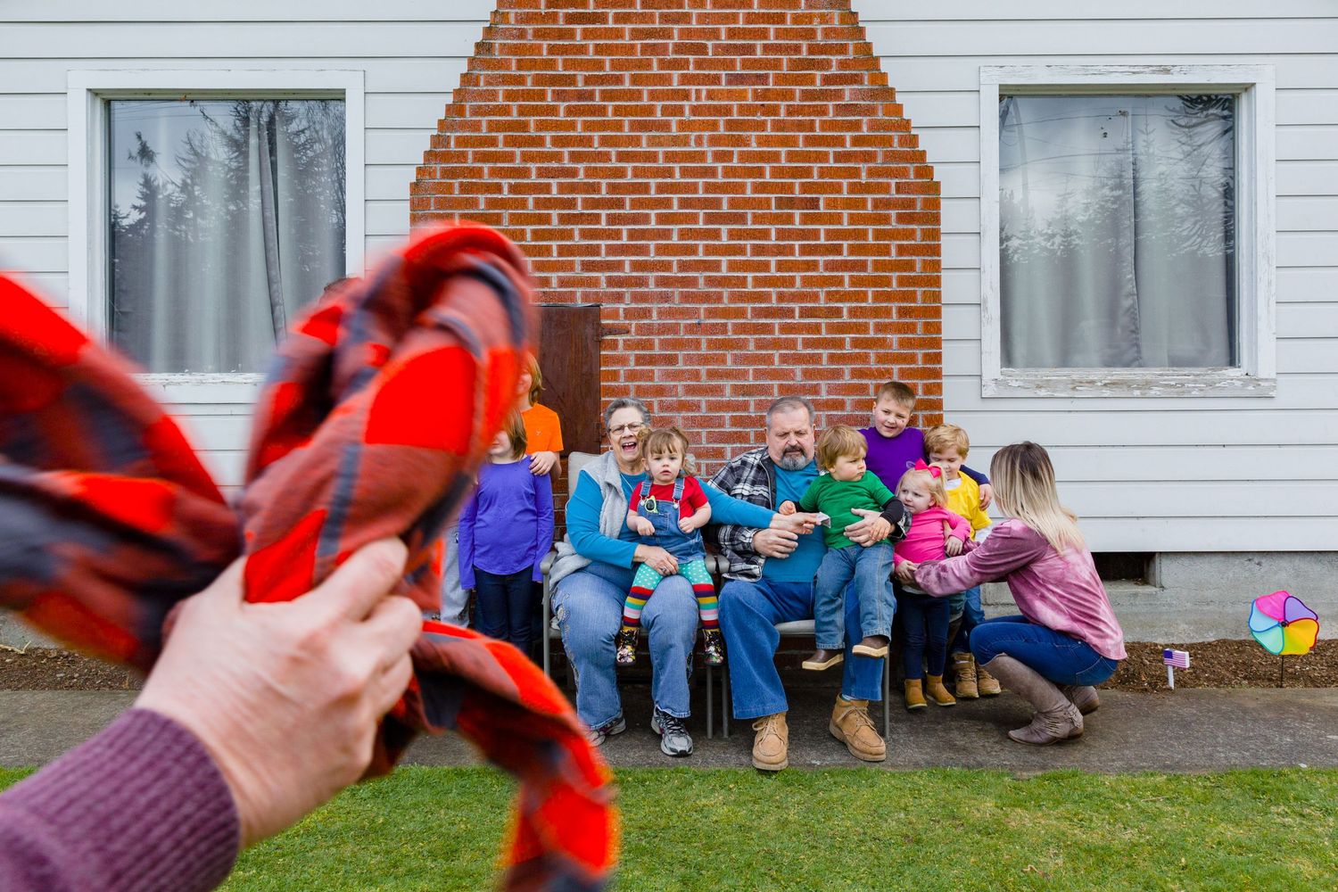 A group sits on outdoor furniture while someone holds up a red object in the foreground.