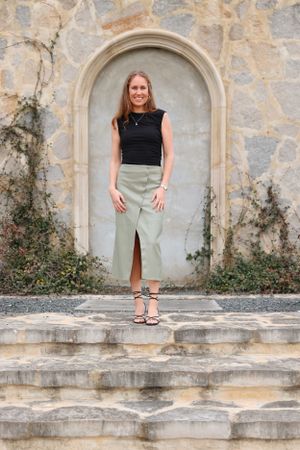 Person standing on stone steps wearing black sleeveless top and sage green skirt.