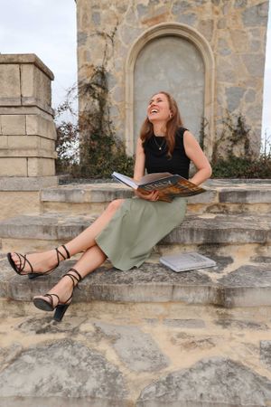 Person sitting on stone steps reading and laughing while holding a book.
