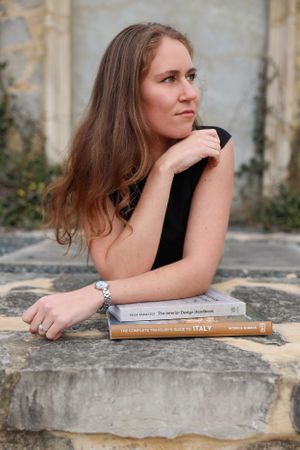 Person posing with travel & interior design books on stone steps with architectural backdrop for personal branding photo session.