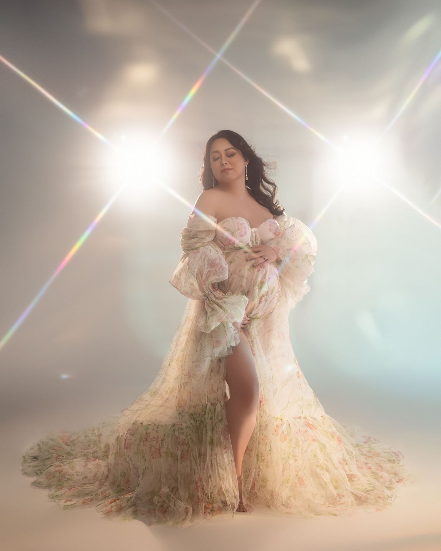 Ethereal portrait in flowing cream-colored gown with ruffled details against bright backlit studio setting with lens flares.