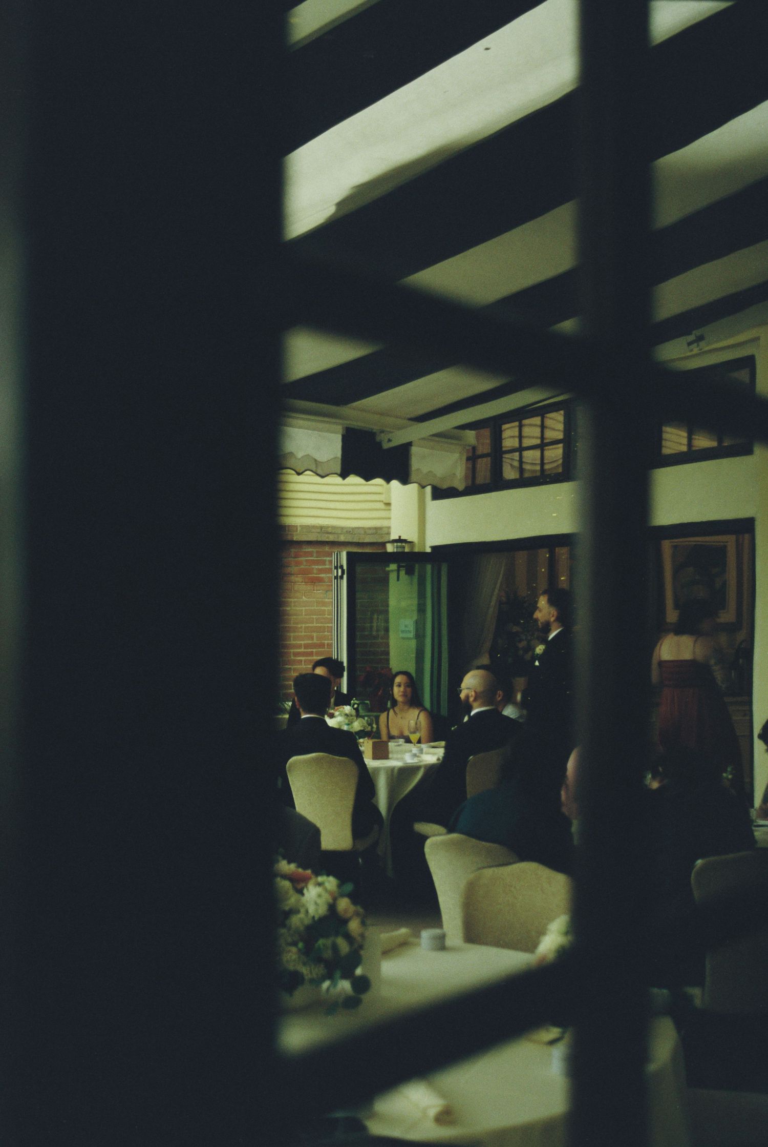 Dark interior hallway with diagonal shadows cast across the space and silhouettes of people visible in the background.