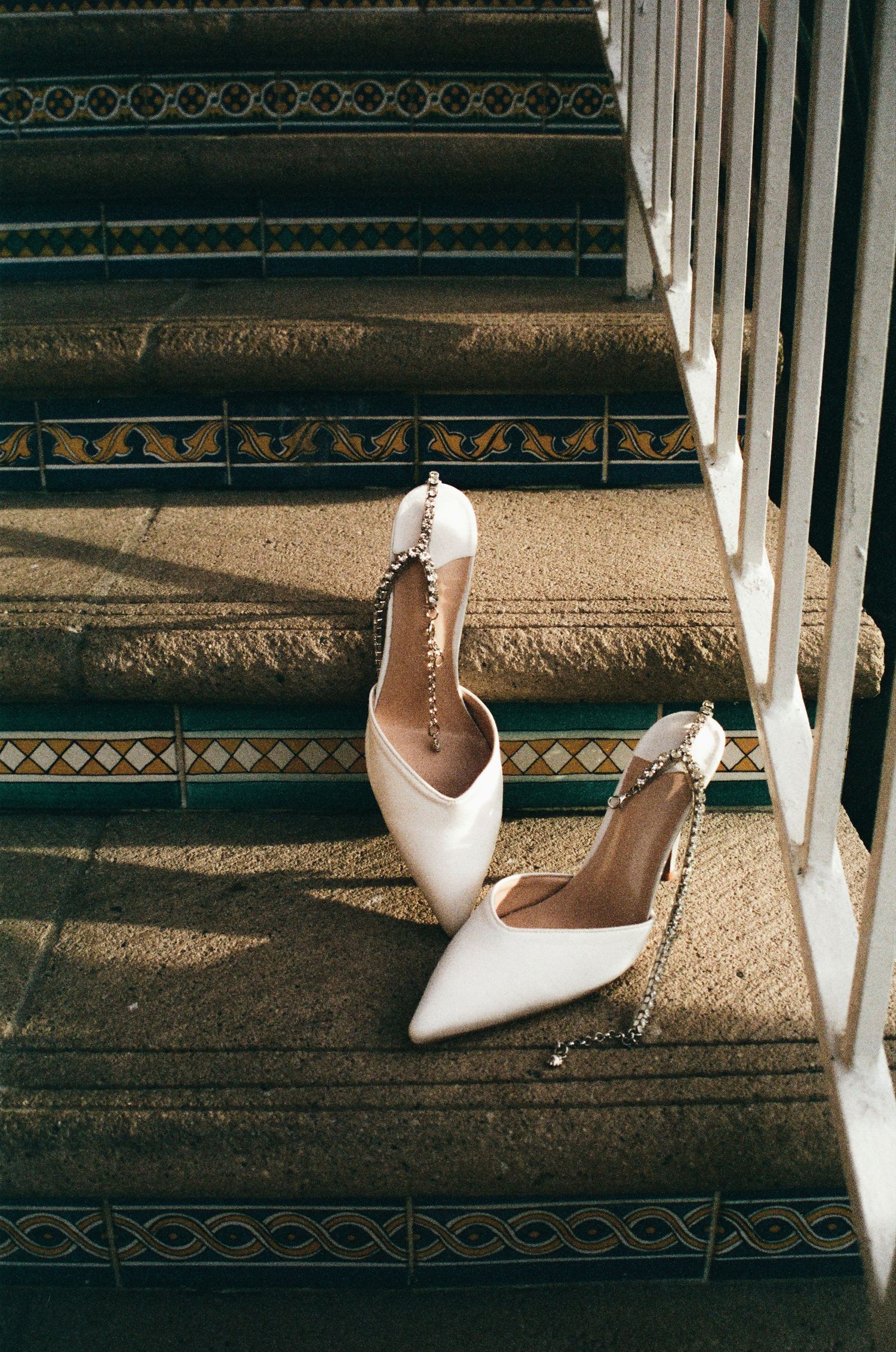 White bridal stiletto heels with pearl straps cast shadows on ornate carpeted stairs in dramatic lighting.