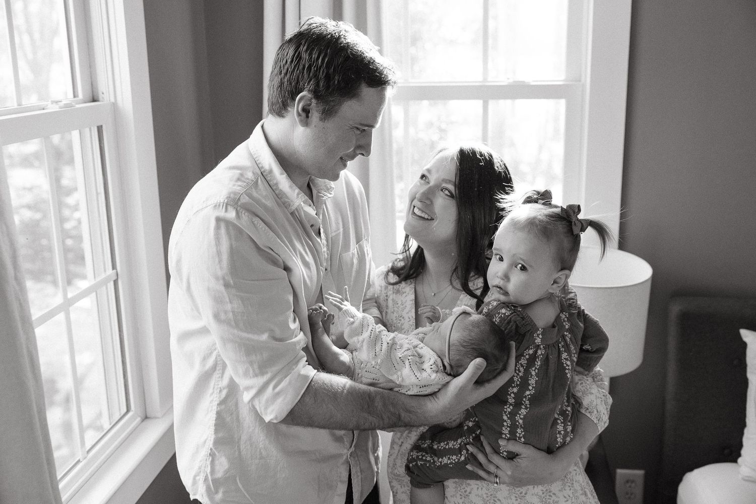 A loving family shares a tender moment together by a bright window in black and white photography.