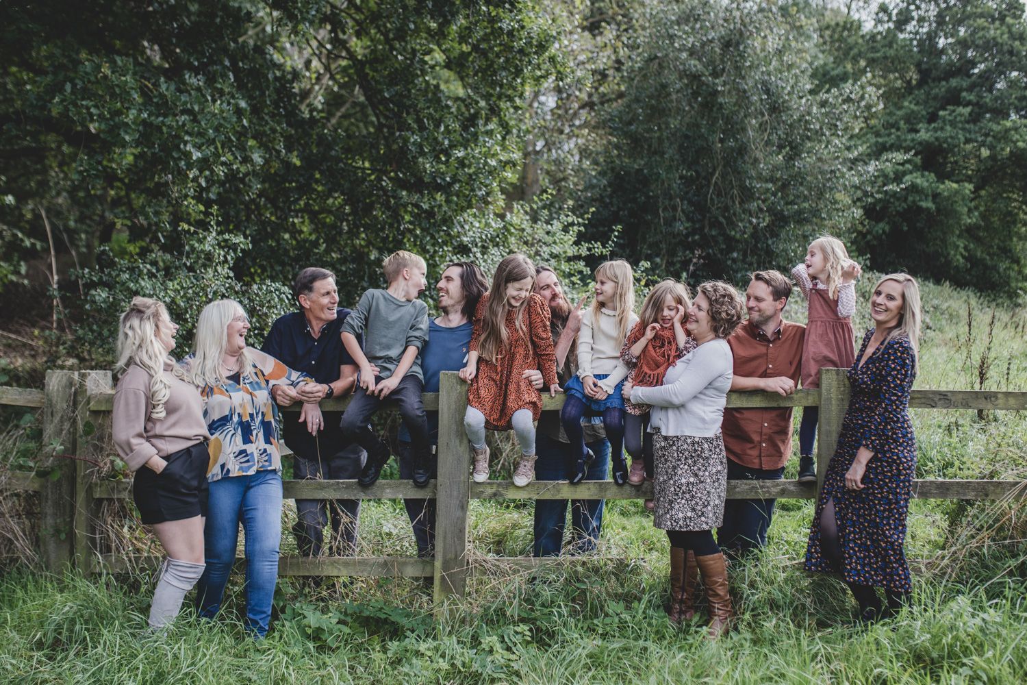 Large group gathering outdoors by a wooden fence in a lush green setting.