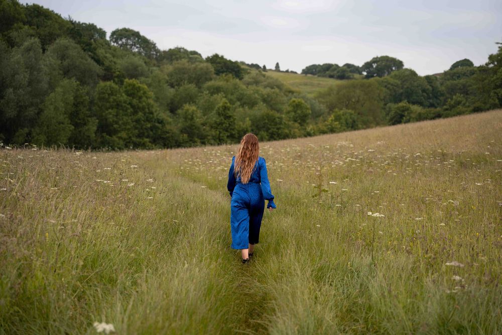 Figure in blue outfit walking through tall grass field with hills in background. Lincolnshire branding photographer.
