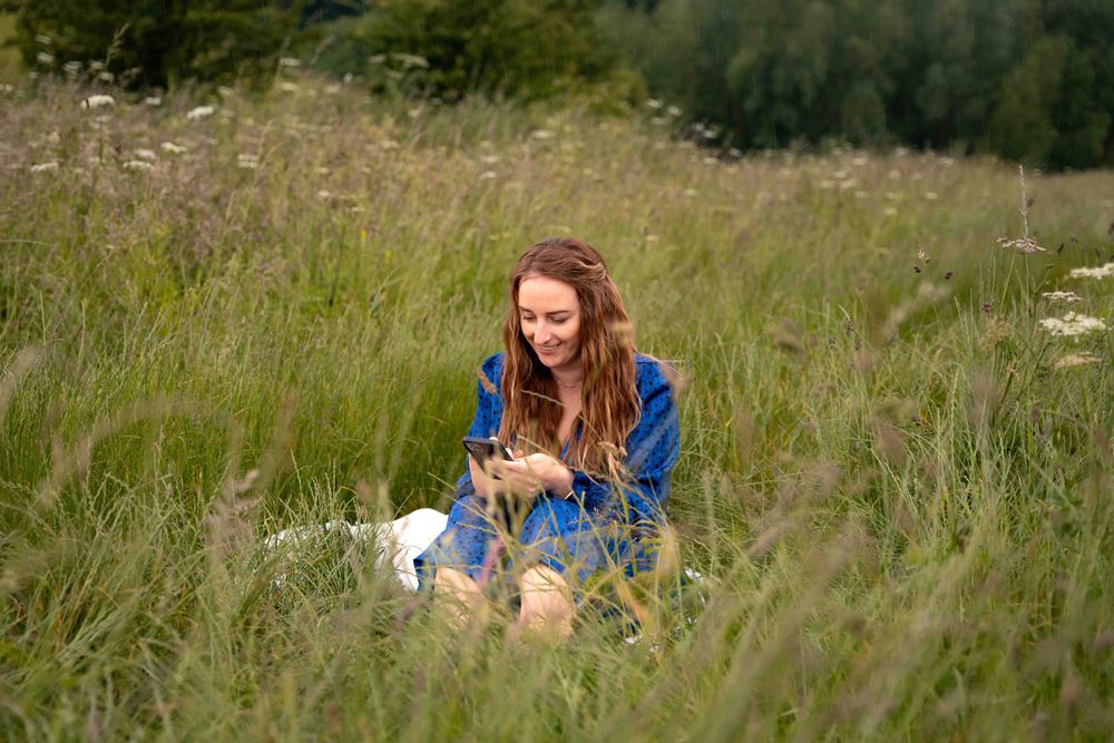 Person in bright blue dress sits among wildflowers in sunny meadow. Lincolnshire branding photographer.