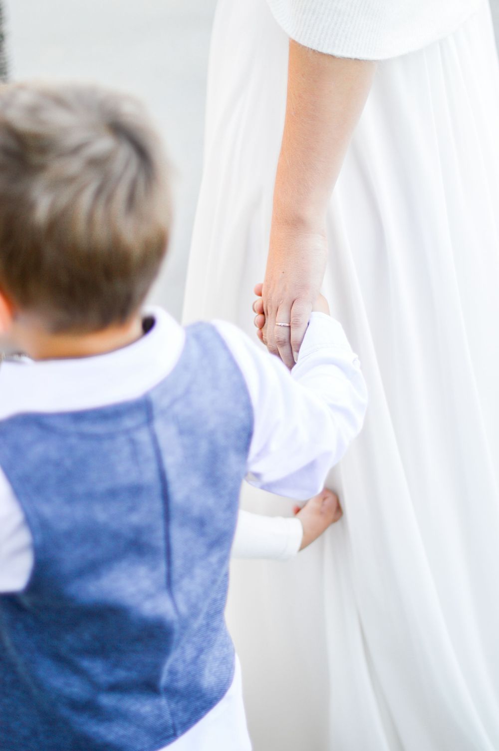 Ein Kind in einem blauen Hemd hält in einem zärtlichen Moment die Hand seiner Mutter an deren Hochzeit.