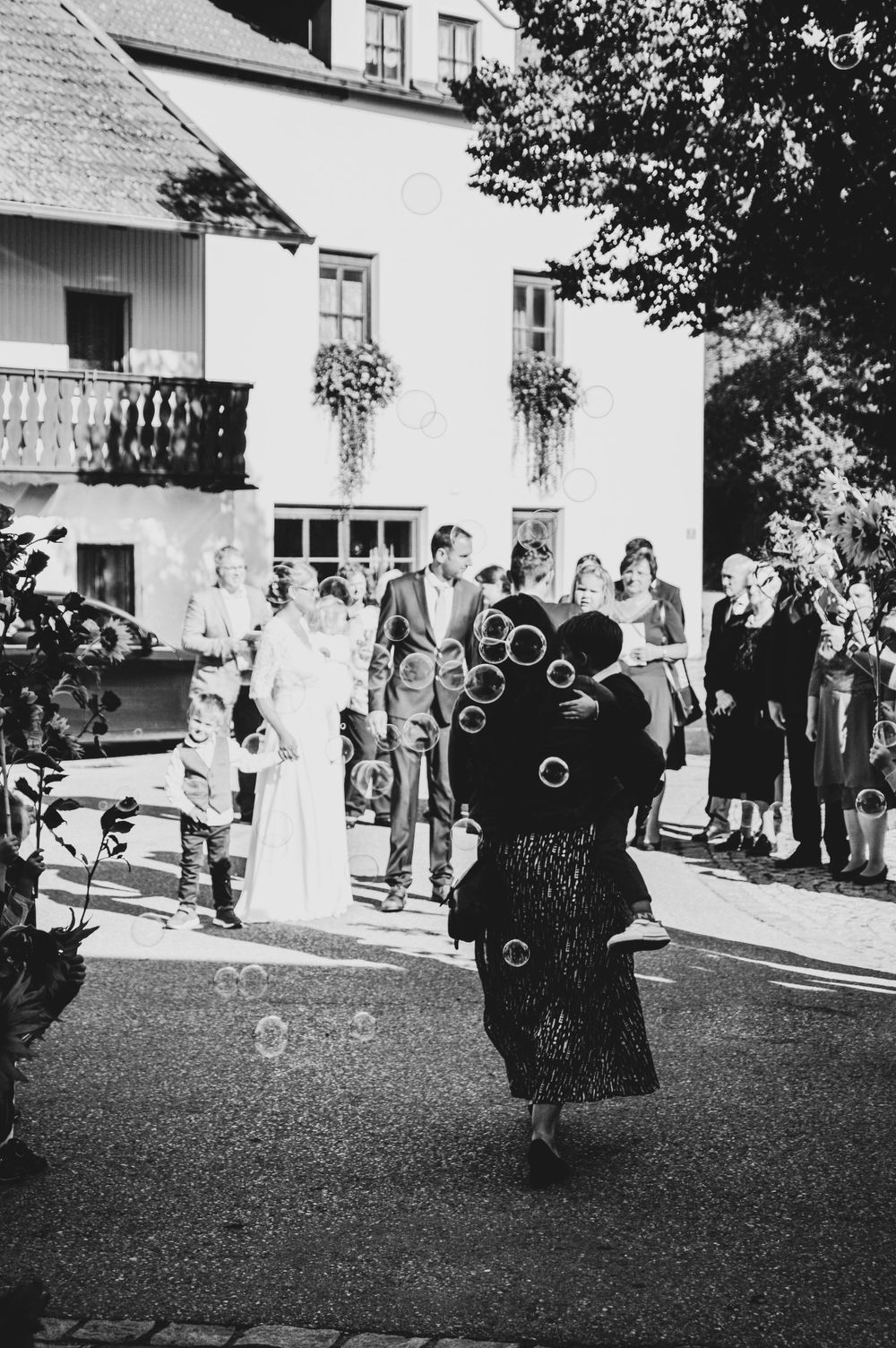 Eine Person in dunkler Kleidung pustet bei einer Veranstaltung im Freien Seifenblasen, während Umstehende in einem Schwarz-Weiß-Foto zusehen