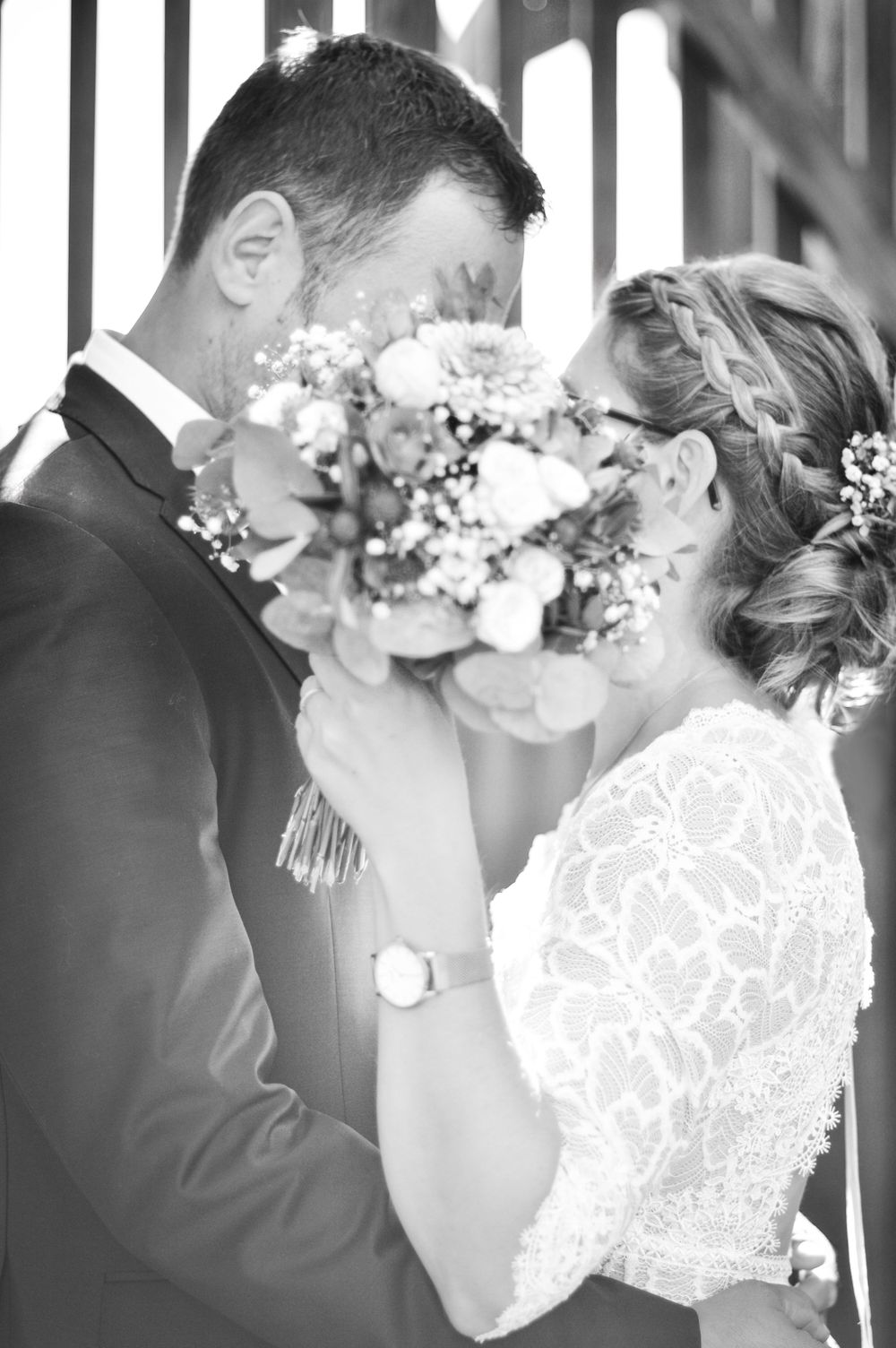 Schwarz-Weiß-Hochzeitsfoto, das ein Brautpaar zeigt, das einen intimen Moment mit einem Blumenstrauß zwischen ihnen teilt.