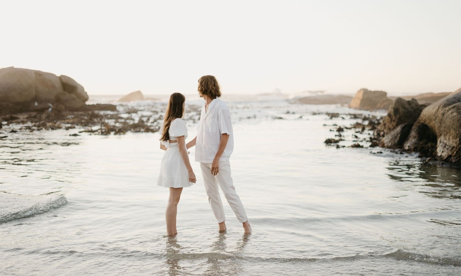 Couple in love surrounded by the beautiful western cape beach scenery with mountains and water in back at Clifton 4th Beach in South Africa