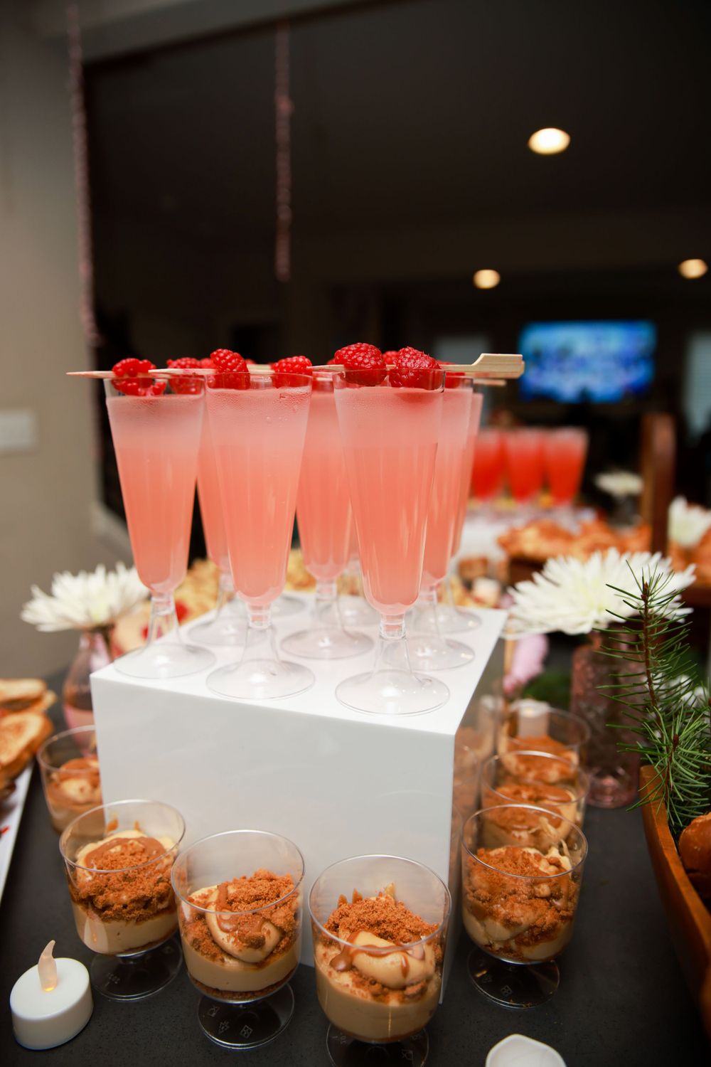 Pink cocktails garnished with raspberries and small desserts displayed on black table.