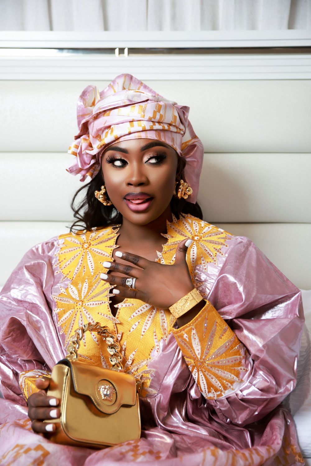 Model wearing pink headwrap and vibrant yellow outfit with gold embellishments against white background.