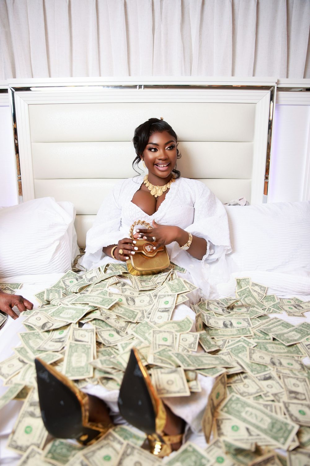 Stylized photo with cash spread across white bedding and gold accessories.