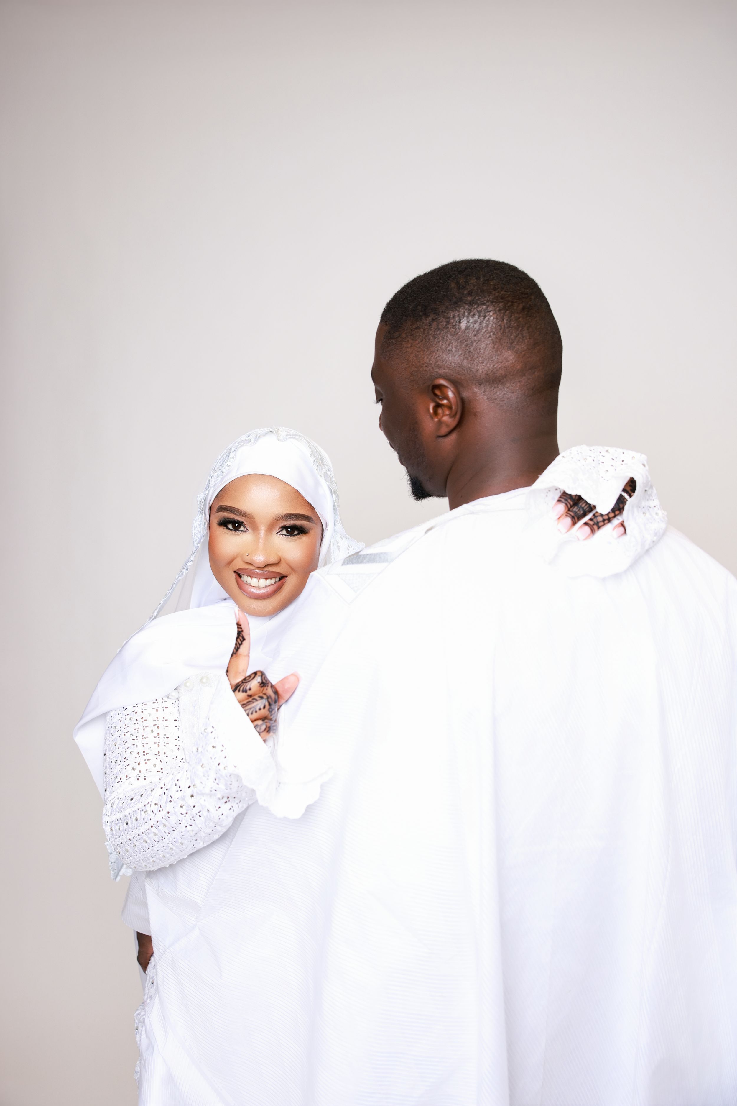 Couple in matching white attire embracing and smiling against neutral backdrop.