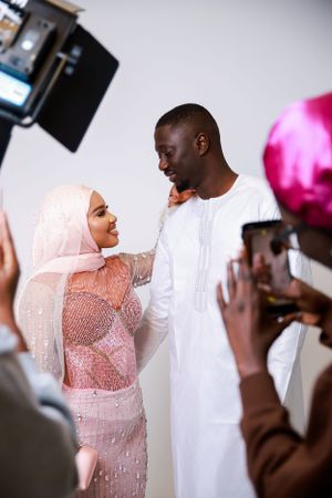 Couple in traditional white and pink attire being photographed during special occasion.