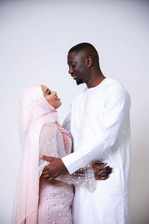 Couple in traditional dress sharing tender moment against light background.