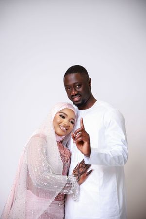 Couple in traditional white and pink attire posing playfully against studio backdrop.