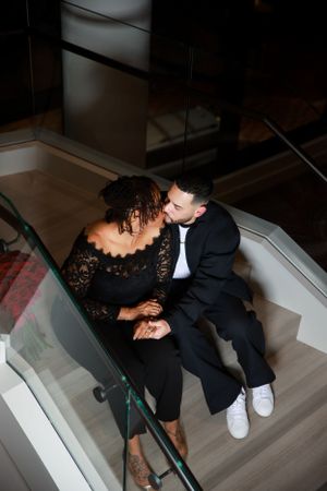 An intimate moment shared on modern stairs in formal black attire and casual white shoes.