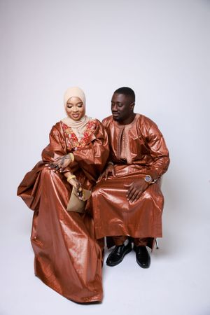 A couple in coordinating rust-colored traditional formal attire sits together against a light background.