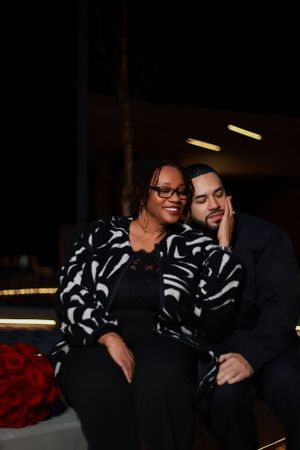 A cozy moment shared on dark furniture with one person wearing a striking black and white patterned jacket.