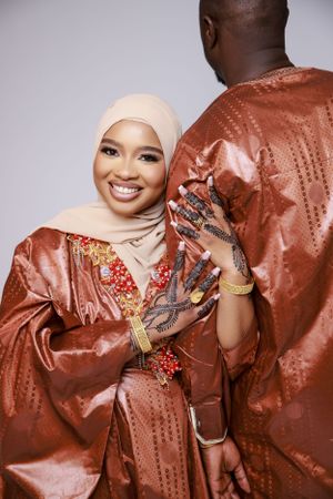 A joyful couple wearing matching rust-colored traditional outfits with gold embellishments and henna-decorated hands.
