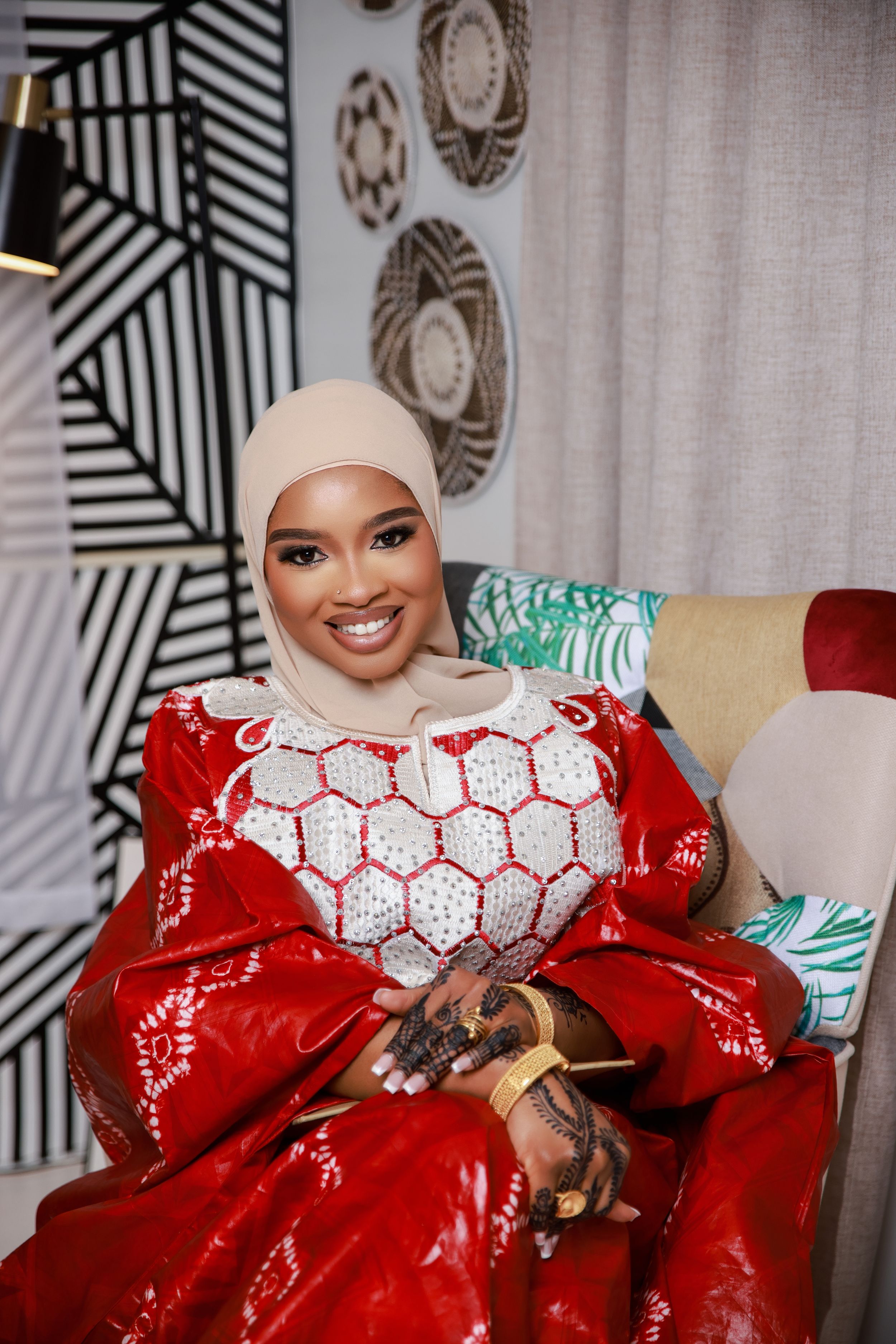 A person wearing a red dress with white hexagonal patterns relaxes on a couch with decorative wall art behind.