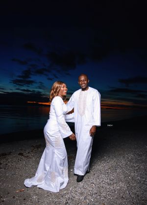 Romantic photoshoot on rocky beach at dusk featuring couple in matching white outfits.