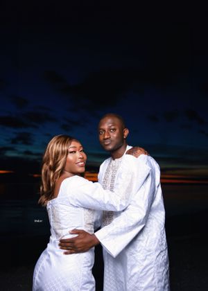 Couple embracing during twilight beach photoshoot in matching white traditional clothing.