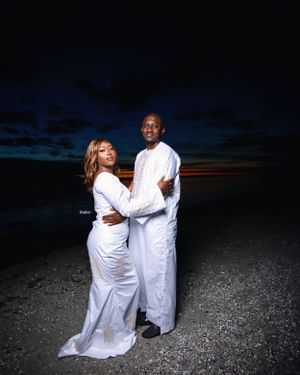 Romantic beach portraits at dusk featuring couple in elegant white traditional attire.