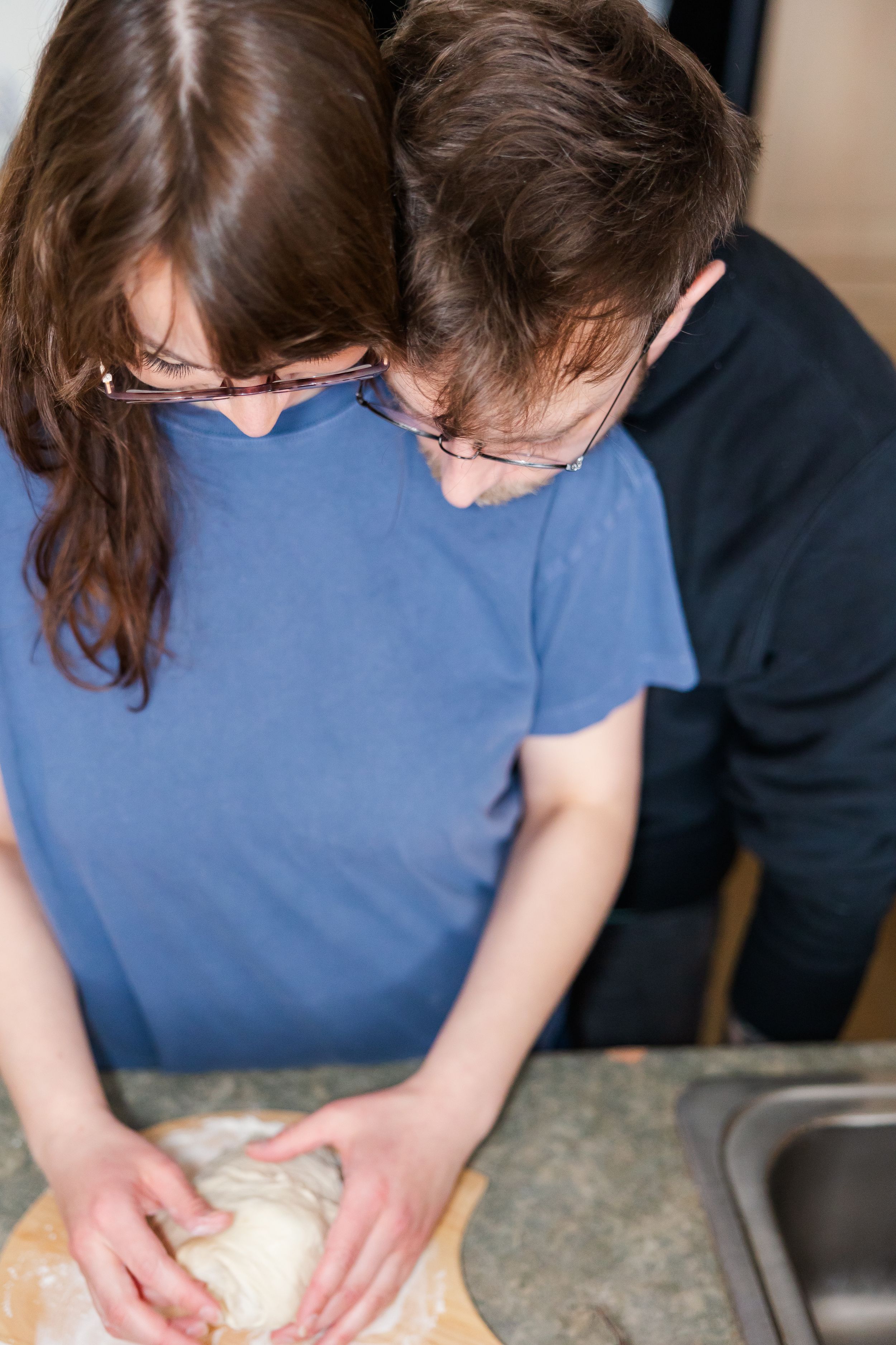 Two people concentrate on kneading dough together at a kitchen counter.