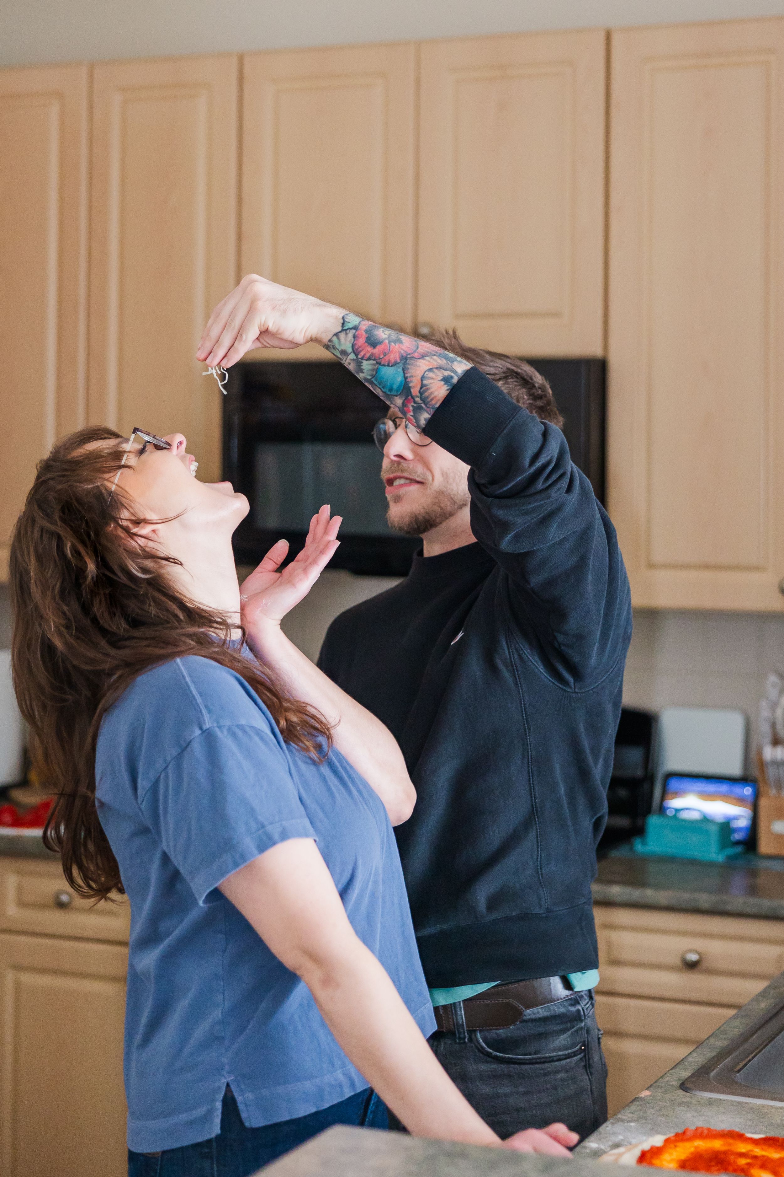 Two people playfully stretching pizza dough in a home kitchen.