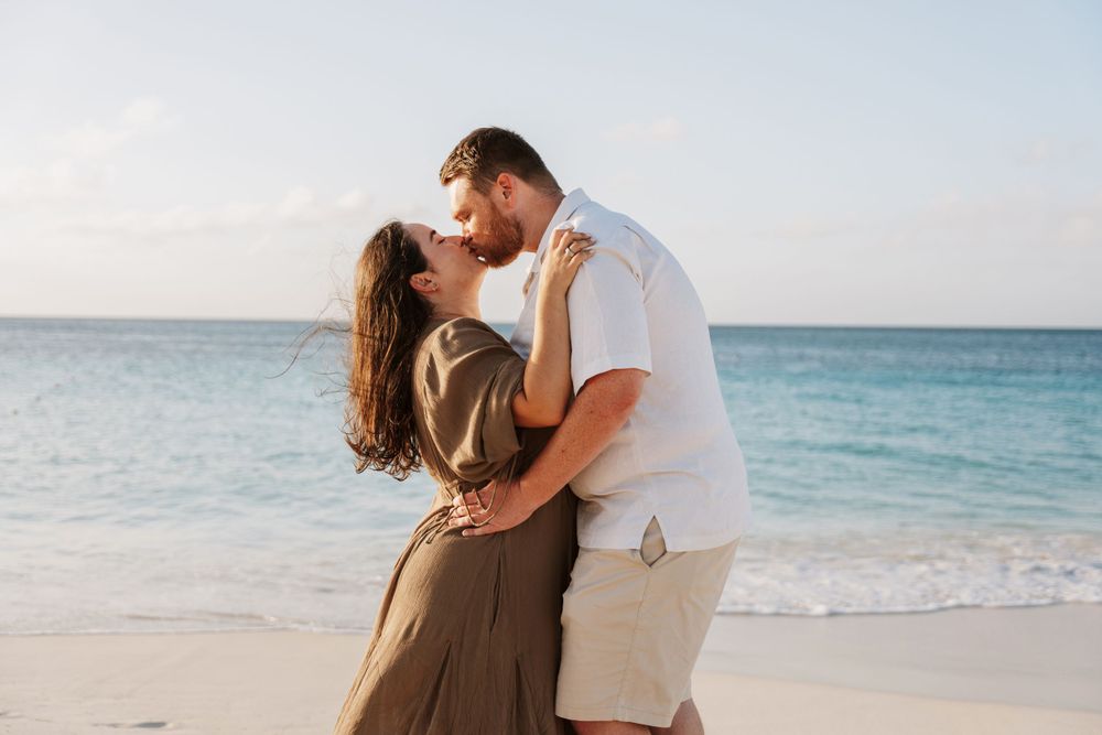 A romantic couple embraces on a sunny beach with turquoise water and white sand in the background.