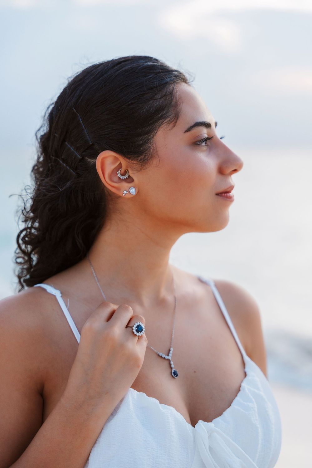 Side profile capture in natural light showing silver jewelry and white dress with curly hair style.