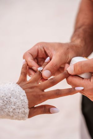 Close-up of hands exchanging a diamond engagement ring during a romantic proposal moment.