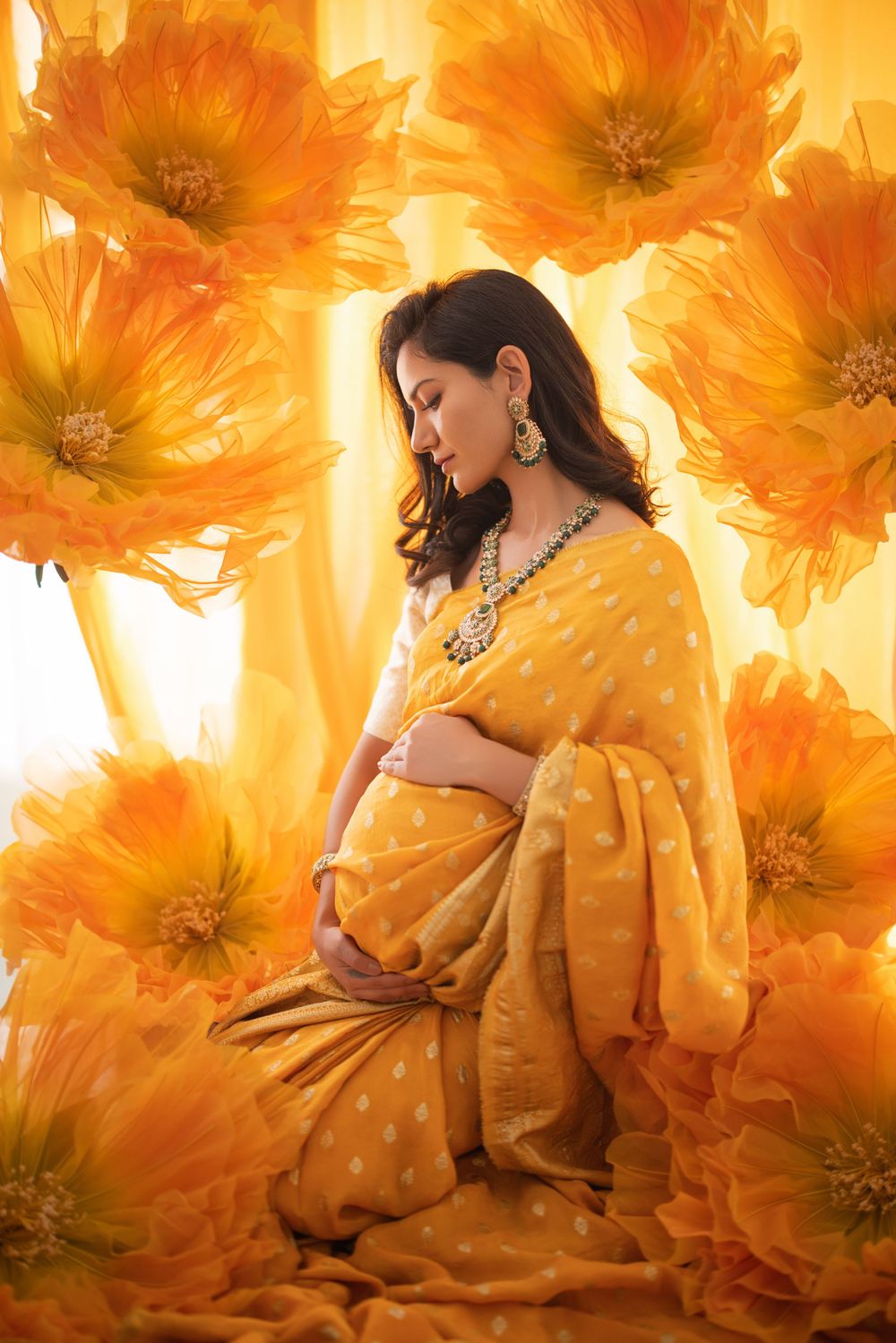 Artistic maternity portrait in yellow sari against dramatic orange floral background.