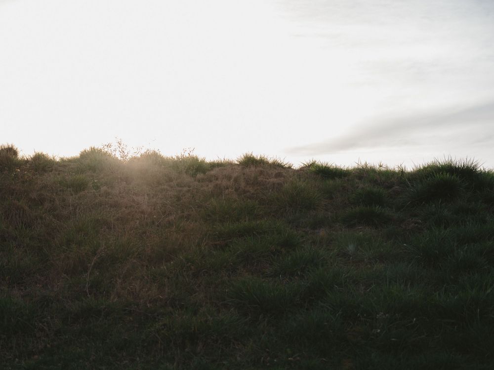 A scenic sunset over rolling hills with dark silhouetted vegetation against a glowing sky.