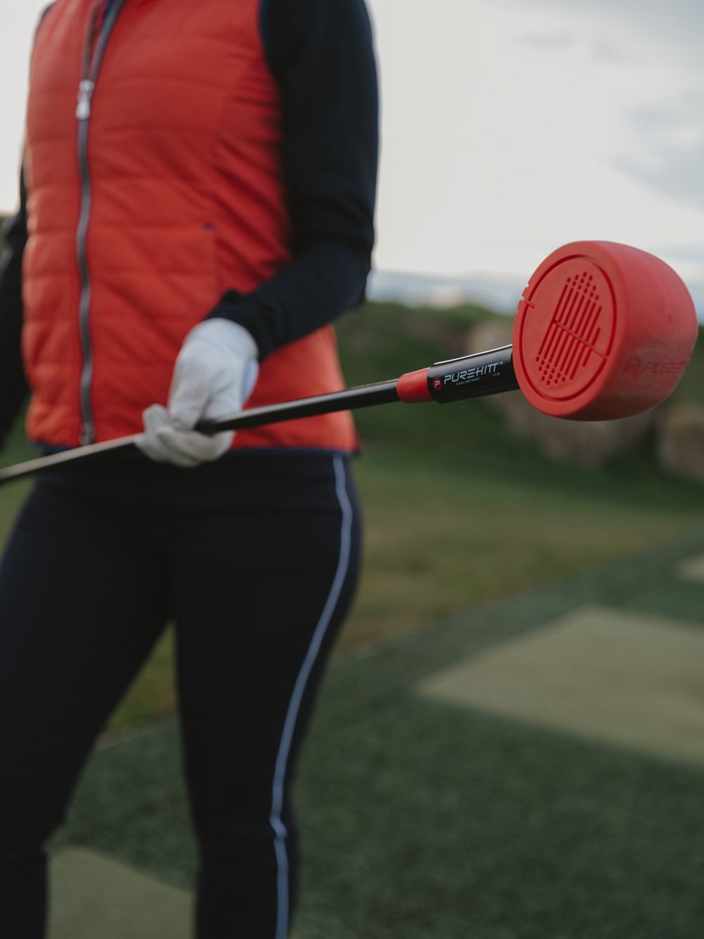 Close-up of a red golf training aid being held against a blurred golf course background.