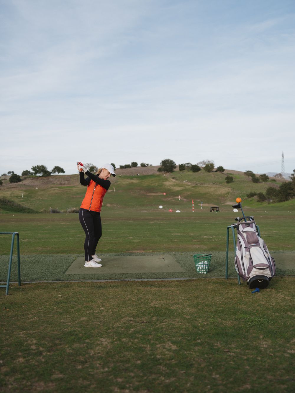 A golfer practicing their swing at a driving range with golf bag and equipment visible.