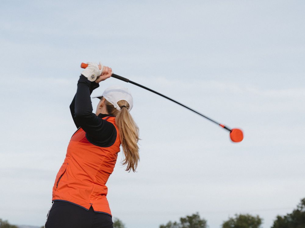 A golfer mid-swing with a red training aid against an overcast sky.