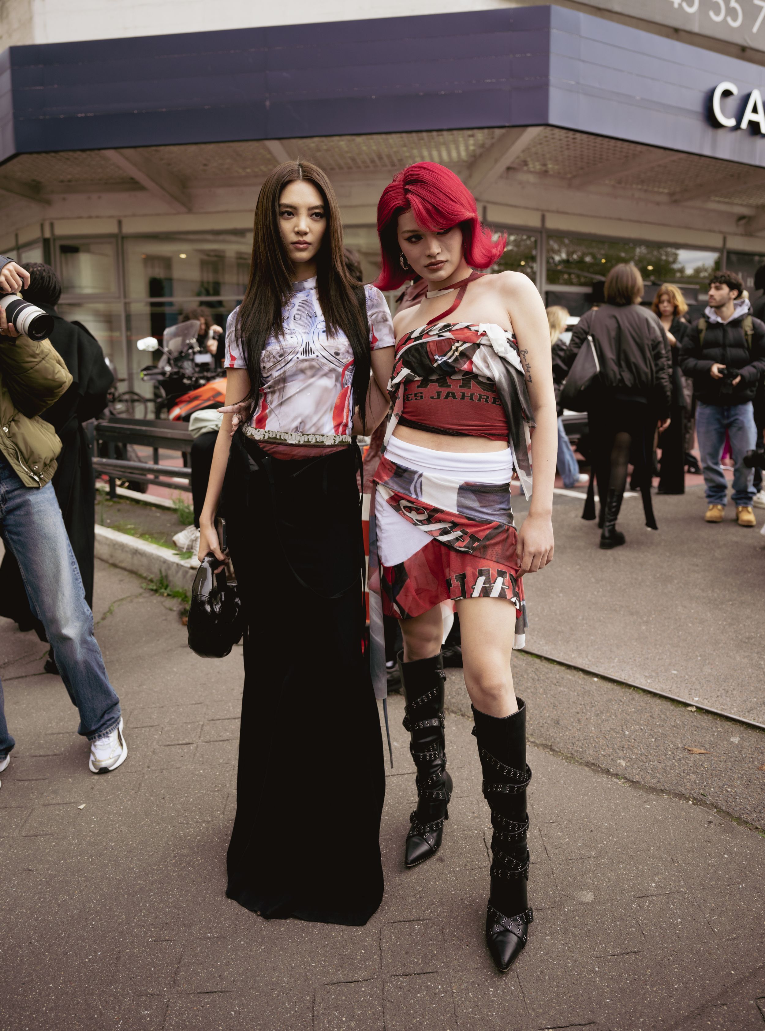 Two streetwear looks mixing graphic prints and edgy accessories outside fashion event.