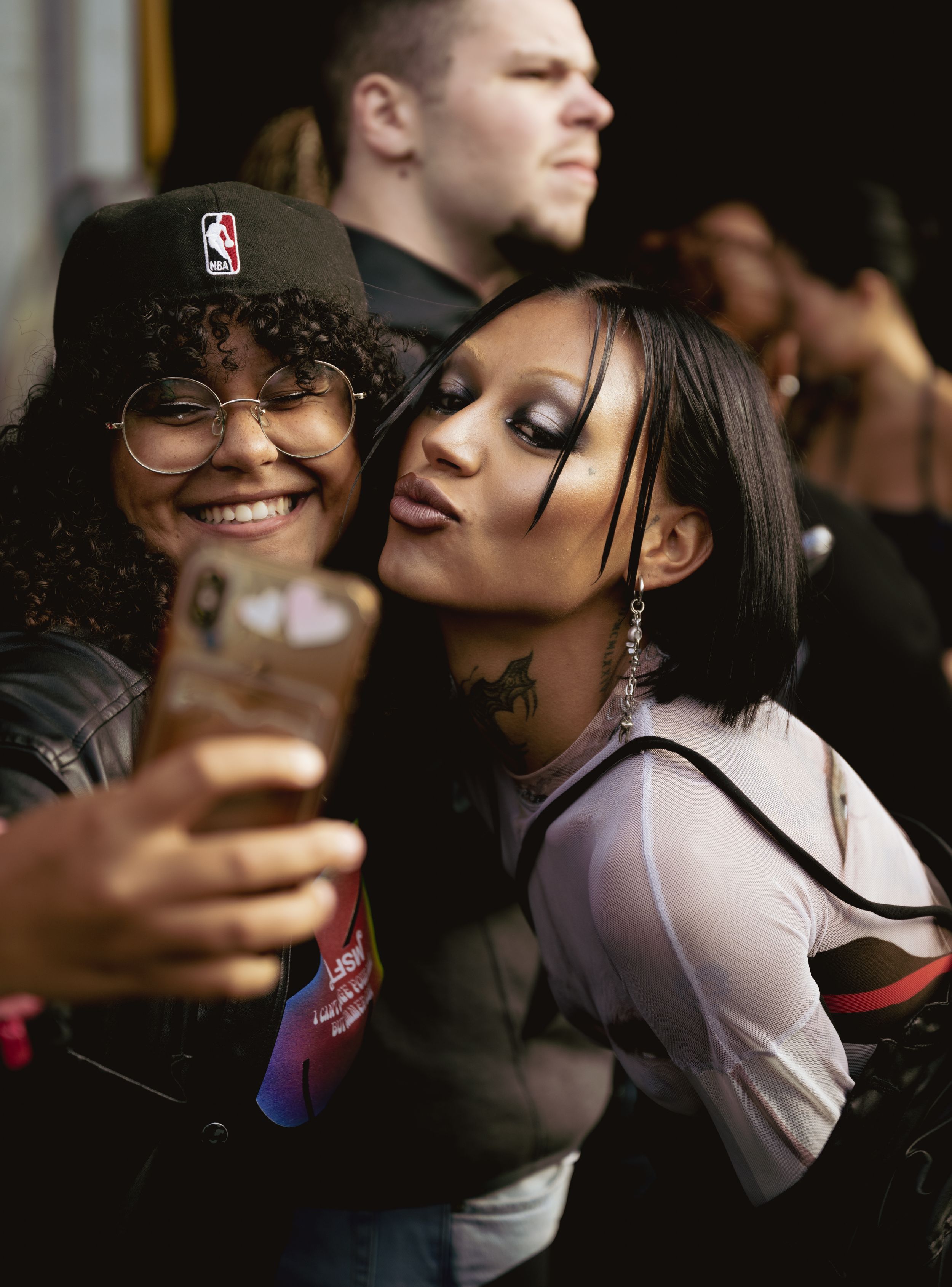 Two friends pose for a playful selfie at a sporting event while wearing casual attire.