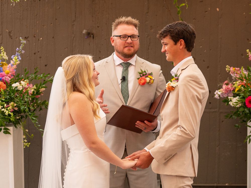 A Tennessee wedding ceremony takes place outdoors with colorful floral arrangements against a brown wall.
