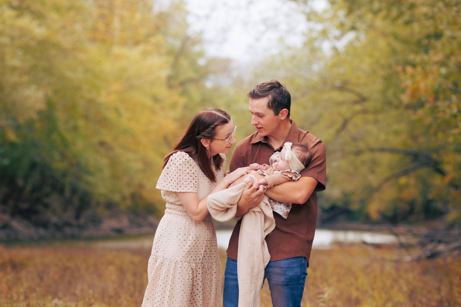 A young family of four standing in the Illinois evening light, surrounded by green grass and pine trees.