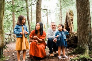 Family of four exploring a forest path together surrounded by tall evergreen trees.
