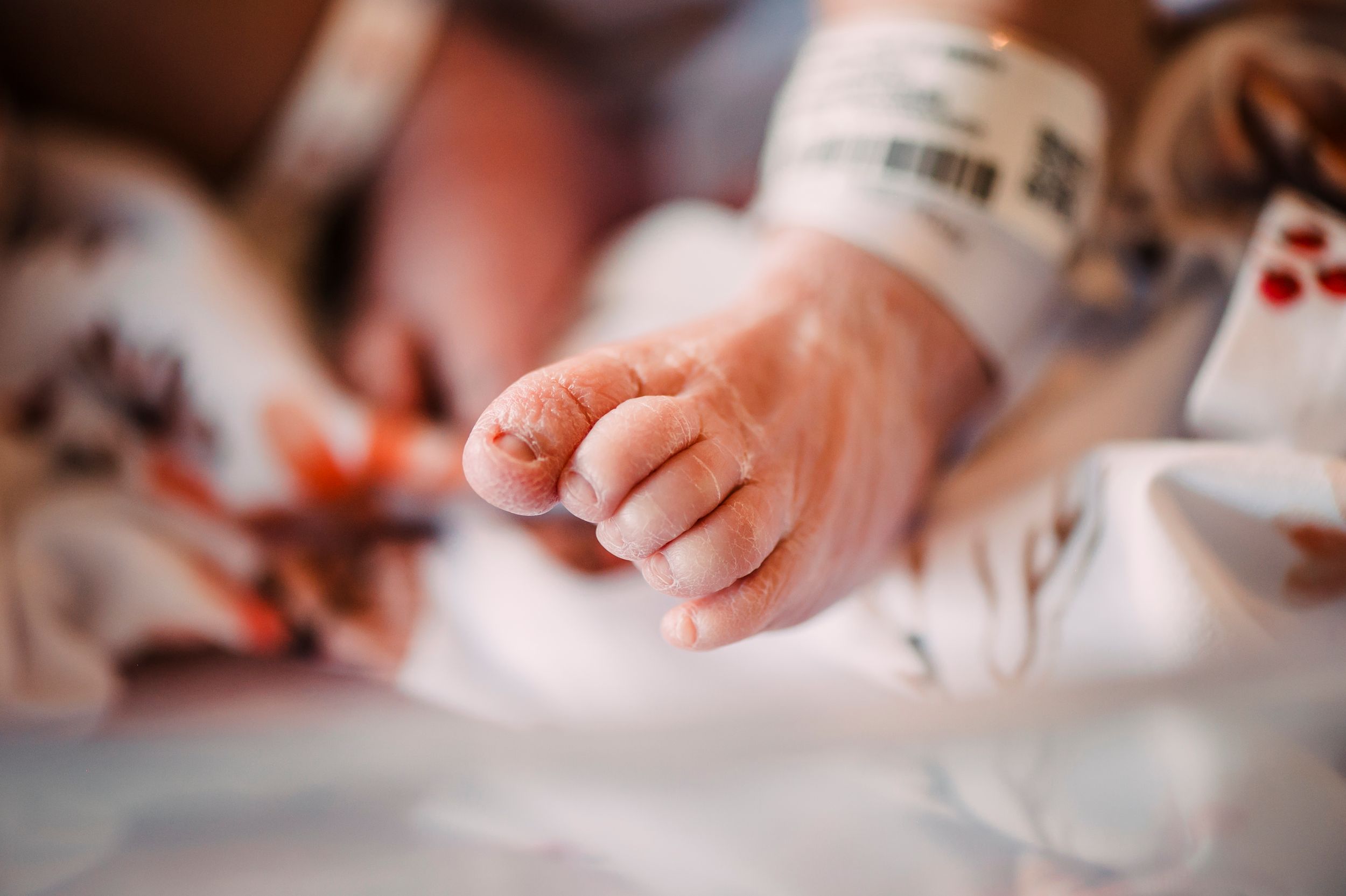 Close-up shot of a tiny newborn baby's hand resting on white hospital bedding.