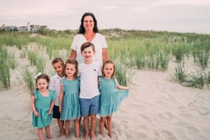 A group stands together on a sandy beach path with coastal grasses and dunes in the background at sunset.