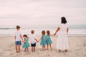 A group holding hands while standing together on a beach at sunset with the ocean waves in the background.