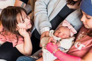Two young children gently observing a newborn baby swaddled in blankets during a tender family moment.
