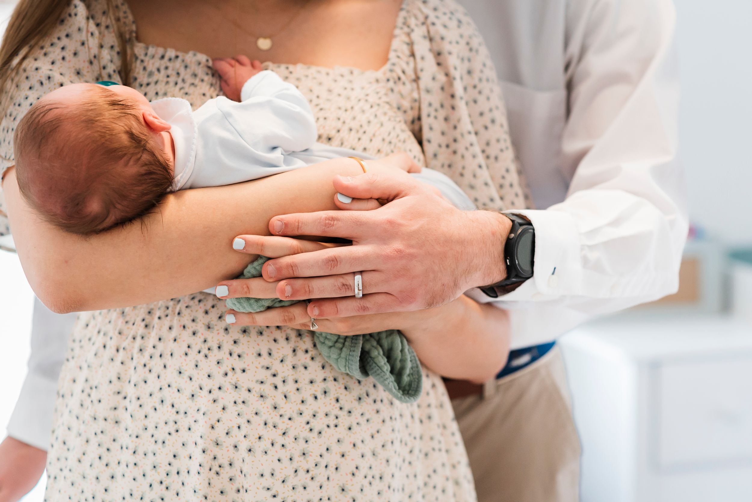 A newborn baby is held in caring arms wearing a white onesie while being gently cradled in a polka dot dress.